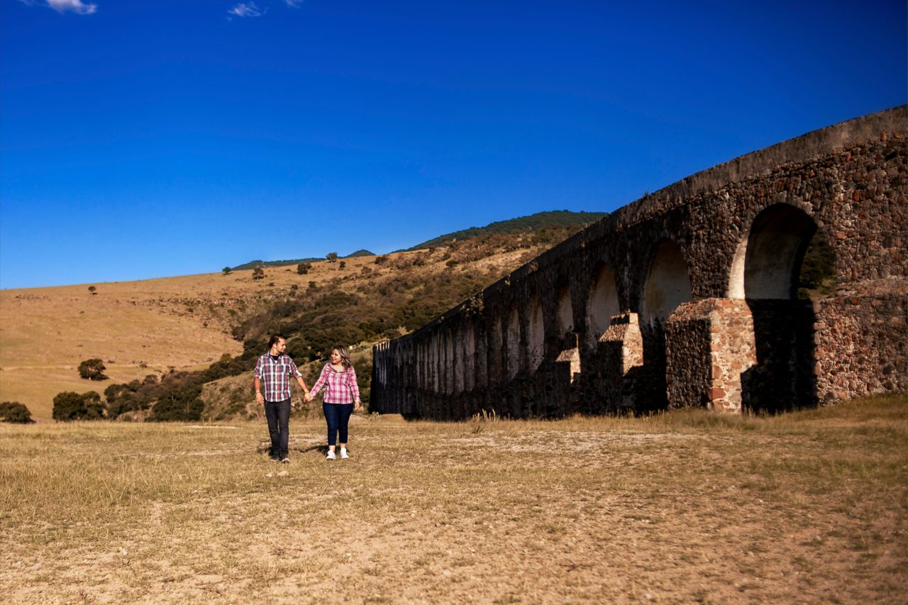Small couple framed by the massive arches of Arcos del Sitio in Mexico during a cinematic pre-wedding session