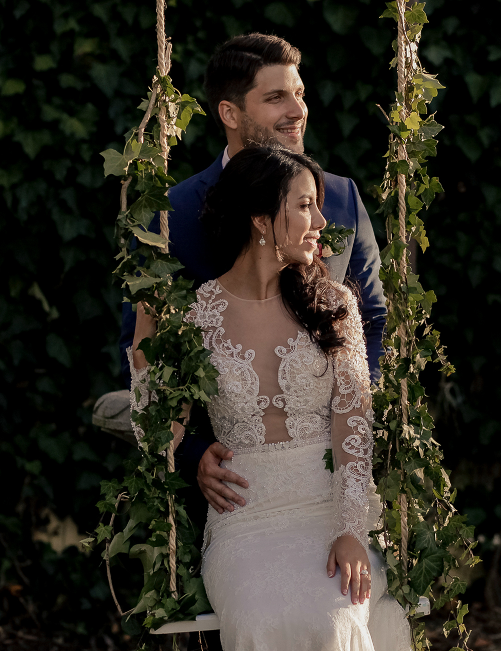 Bride sitting on a floral swing with groom behind her, both looking away, destination wedding session in Ecuador